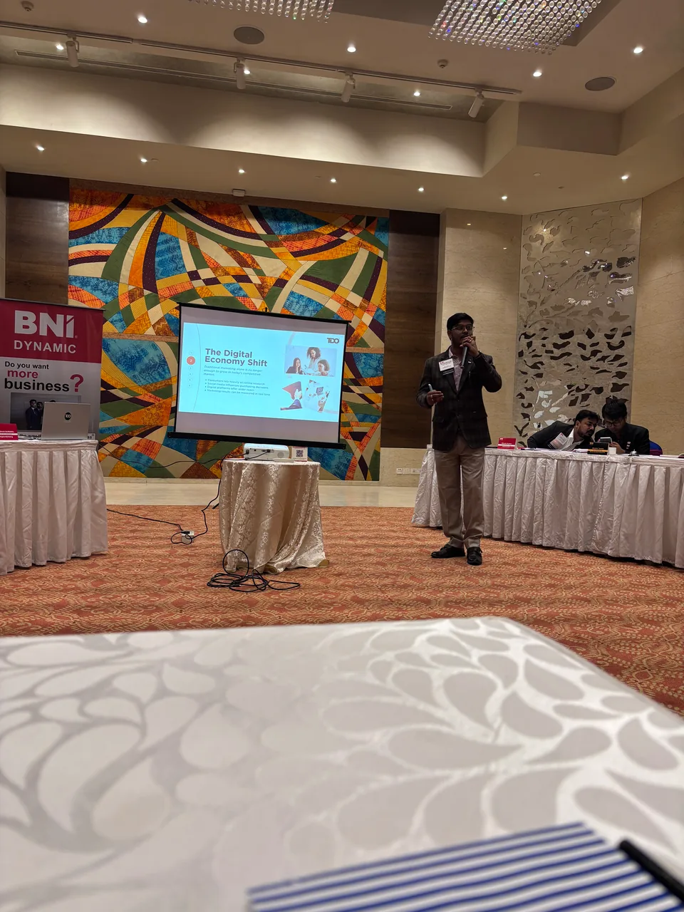 Roshan Burnwal speaking beside a presentation slide titled The Digital Economy Shift at a BNI Dynamic meeting.