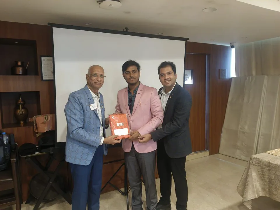 Roshan Burnwal standing with two attendees while they hold a BNI item at a gathering.
